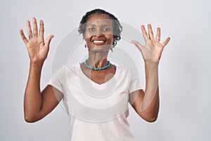 African woman with dreadlocks standing over white background showing and pointing up with fingers number ten while smiling