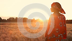 African woman farmer in traditional clothes standing in a field of crops in Africa at sunset or sunrise