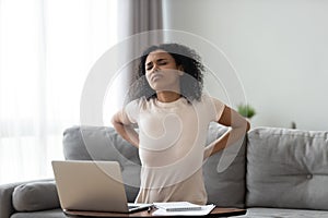 African woman feeling backpain tired of computer sit on sofa