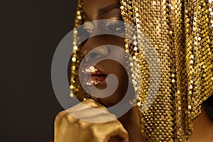 African woman with gold metallic make-up and full shiny lips looking away holding chin, close up