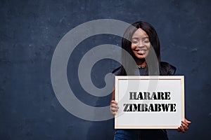 African woman hold white board with Harare Zimbabwe inscription. Most populous city in Africa concept
