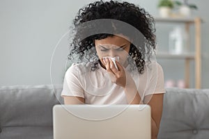 African woman holding handkerchief blowing runny nose working on laptop photo
