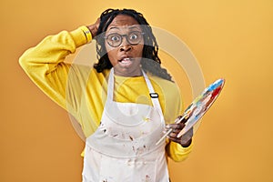 African woman holding painter palette crazy and scared with hands on head, afraid and surprised of shock with open mouth