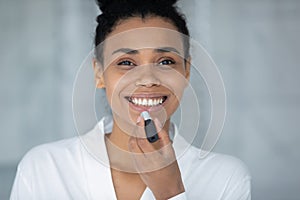 African woman looking at camera applying lipstick on lips