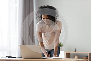 African woman looking at computer writing down useful important information photo