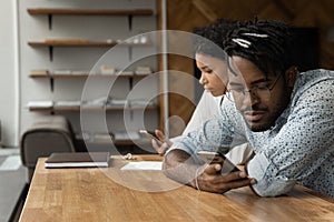 African woman and man sit at table with smartphones devices