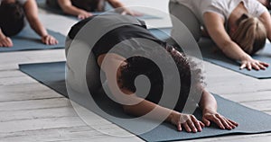 African woman performing Child pose with associates during yoga class