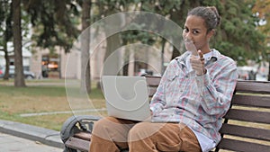 African Woman Pointing at Camera while Sitting on Bench Outdoor