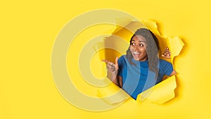 African Woman Pointing Finger Aside Through Torn Yellow Paper Background