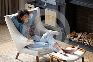 African woman put feet on footstool relaxing on cozy armchair