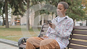 African Woman Reacting to Loss on Smartphone while Sitting Outdoor on Bench