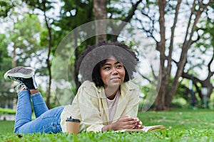 African woman read a book in the park. Student girl lie down and reading book in the park