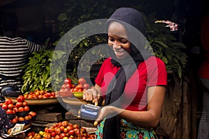 African woman selling food stuff in a local market smiling while using a mobile point of sale device