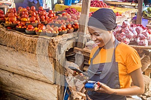 african woman selling in a local african market holding a mobile point of sale system and using her mobile phone