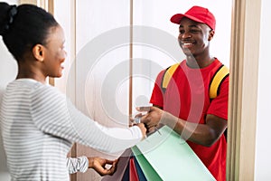 African Woman Shopaholic Receiving Shopping Bags From Cheerful Deliveryman Indoor