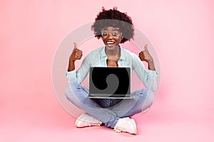 African Woman Showing Laptop Screen Sitting Gesturing Thumbs-Up, Pink Background