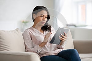 African woman sit on couch using tablet gadget