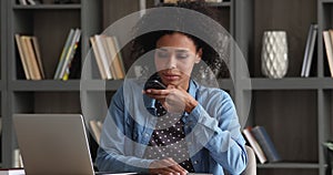 African woman sit at workplace chatting to colleague on speakerphone