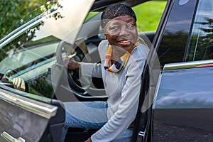 African woman sitting in electric car with open door.