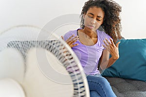 African woman suffering from heat in front of fan at home