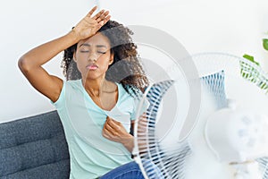 African woman suffering from heat in front of fan at home