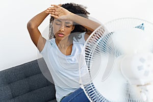 African woman suffering from heat in front of fan at home