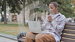 African Woman Surprised by Online Success while Sitting Outdoor on Bench