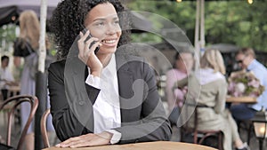 African Woman Talking on Phone, Sitting in Outdoor Cafe