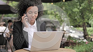 African Woman Talking on Phone while Sitting in Outdoor Cafe