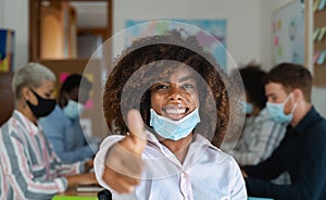 African woman thumb up wearing face mask in co-working creative space with team work - Young people working during corona virus