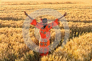 African woman in traditional clothes arms raised in field of crops at sunset or sunrise