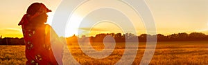 African woman in traditional clothes in field of crops at sunset or sunrise panorama