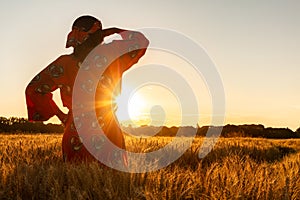 African woman in traditional clothes standing in a field of crops at sunset or sunrise