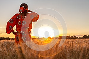 African woman in traditional clothes standing in a field of crops at sunset or sunrise