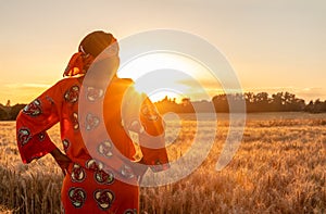 African woman in traditional clothes standing in a field of crops at sunset or sunrise