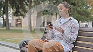 African Woman Upset by Online Shopping Failure while Sitting Outdoor on Bench