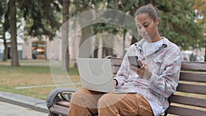 African Woman Using Smartphone and Laptop while Sitting Outdoor on Bench