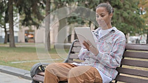 African Woman using Tablet while Sitting Outdoor on Bench