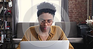 African woman wear eyeglasses sit at desk texting on laptop