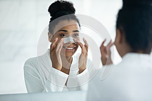 African woman looking in mirror applying cleansing nose strip