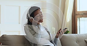 African woman wearing wireless headphones relaxing listening music on phone