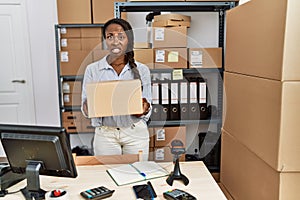 African woman working at small business ecommerce holding box clueless and confused expression