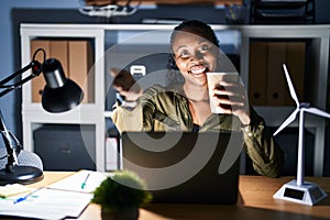 African woman working using computer laptop at night smiling cheerful offering palm hand giving assistance and acceptance