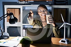 African woman working using computer laptop at night smiling friendly offering handshake as greeting and welcoming