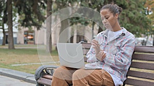 African Woman with Wrist Pain Using Laptop while Sitting Outdoor on Bench