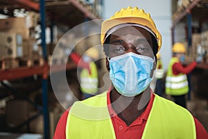 African worker man looking at camera inside warehouse while using safety mask - Focus on face