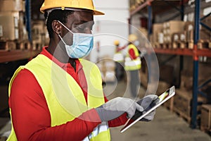 African worker man using tablet inside warehouse while wearing safety mask - Focus on face