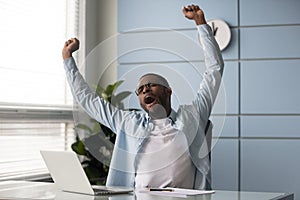 African worker raised hands stretches yawning seated on chair indoors