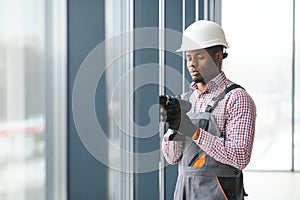 African Workman in overalls installing or adjusting plastic windows in the living room at home