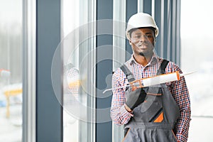 African Workman in overalls installing or adjusting plastic windows in the living room at home